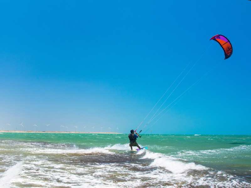 Duas pessoas na praia de Icaraizinho observando praticante de kitesurf no oceano sob céu azul claro