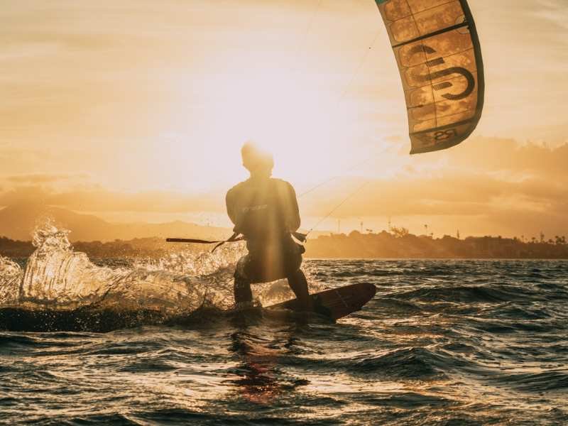 Praticante de kitesurf executando curva acentuada em onda de Icaraizinho com palmeiras e turbinas eólicas ao fundo