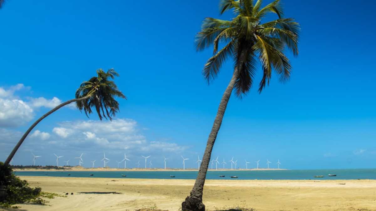 Praia de Icaraizinho ao entardecer com silhuetas de turbinas eólicas e reflexo do sol na areia molhada