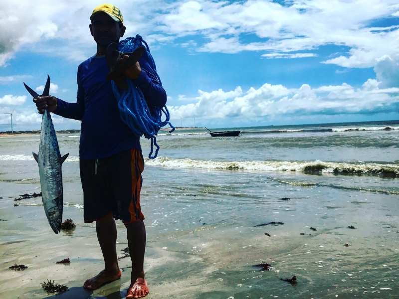 Pescadores segurando um peixe na praia de icaraizinho com mar ao fundo