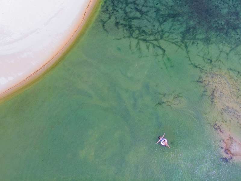 Carro estacionado na faixa de areia da Praia de Caetanos, cercado por coqueiros em dia de sol
